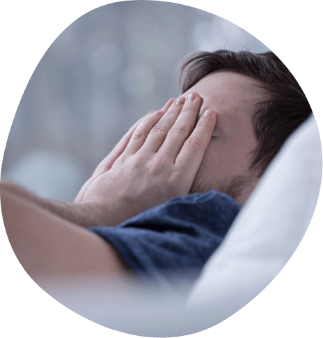Man lying in bed covering his face with his hands